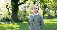 Lächelnde Frau mit grünem Pullover und weißem Hemd im sonnigen Garten