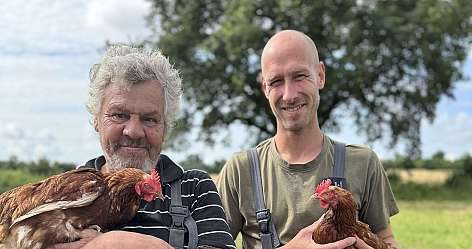 Zwei Männer halten Hühner in einem Feld.