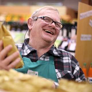 Ein Verkäufer hält eine Tüte und lächelt freundlich.